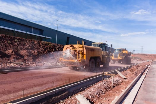 Roadworks construction preparation by industrial vehicles water spraying road surface for asphalt.