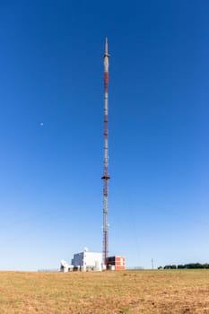 Communications signal tower tall high steel structure,on high ground hilltop for radio tv mobile phones against blue sky.
