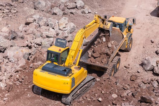 Industrial excavator machine loading construction truck vehicle heavy rock earthworks.