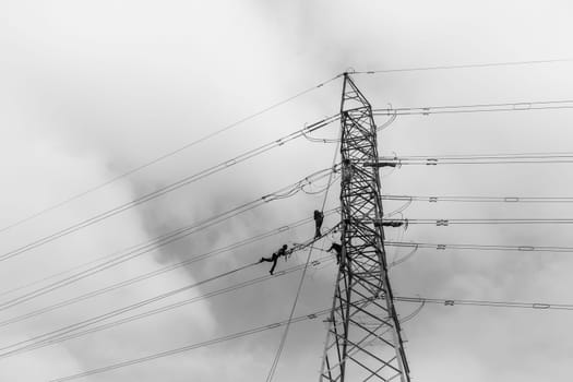 Electricians high rigging working maintnance on electrical cable power lines on steel tower structure.