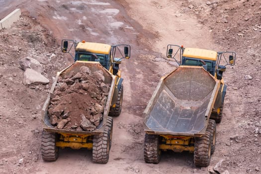 Industrial earthworks loading truck vehicles heavy rocks on construction site overhead photo.