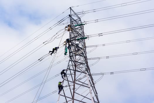 Electricians high rigging hanging on steel cables high above ground working on electrical cable power lines repairs on steel tower.