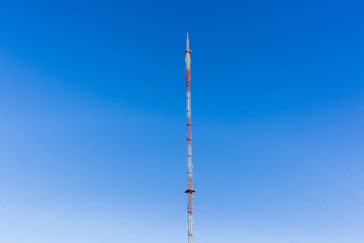 Communications signal tower tall high steel structure,on high ground hilltop for radio tv mobile phones against blue sky.