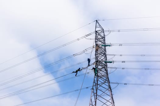 Electricians high rigging working maintnance on electrical cable power lines on steel tower structure.