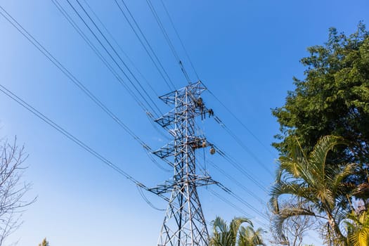 Electricians unidentified men high up suspended on electrical steel tower rigging installing new high voltage electricity power-lines.