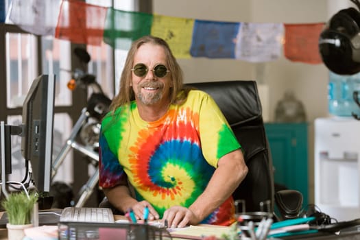 Smiling man in tie dye shirt and round glasses at his desk
