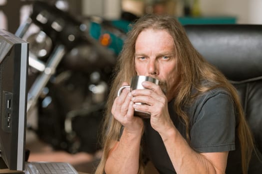 Sleepy man at his desk with a coffee and motorcycle in the background