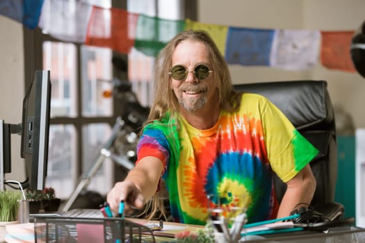Smiling man in tie dye shirt and round glasses at his desk