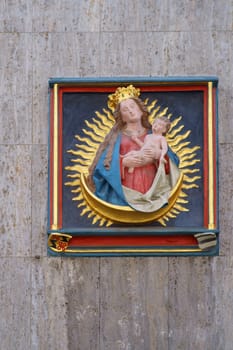 Mainz, Germany - May 27, 2019: The gilded relief of Mother Mary with the Jesus child and a radiate wreath on the outer facade of a building in the cathedral street on May 27, 2019 in Mainz.