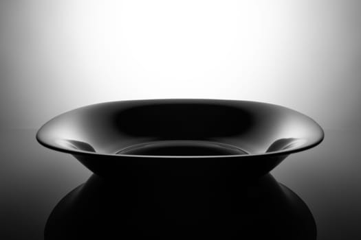 Empty black soup plate, isolated in the shadows.