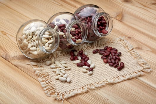 Various types of dry haricots in glass jars lying on wooden background. Different kinds legumes.
