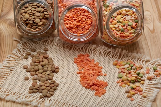Various types of dry lentils in glass jars lying on wooden background. Different kinds legumes.