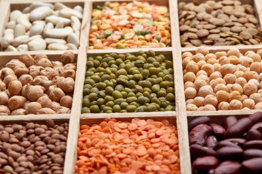 Background from various kinds legumes. Different varieties of legumes in a wooden box. Dry haricots, lentils, peas, chickpeas, mung beans. Top view.