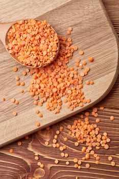 Orange dry lentils on wooden spoons lying on wooden background. Legumes. Top view.