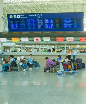 FRANKFURT AM MAIN, GERMANY - AUGUST 29, 2018: Frankfurt international airport terminal, woman with luggage cart, passengers waiting on chairs under time table