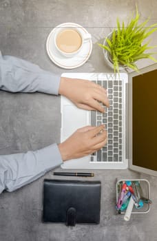 Top view of businessman working using laptop with coffee, potted plant, notebook and business accessories on the desk