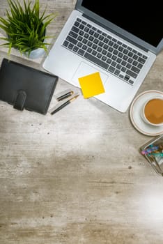 Top view of business desk with laptop, notebook, sticky notes, coffee, potted plant and business accessories on the office