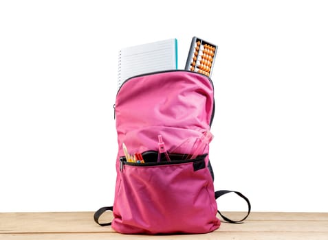 Pink backpack with book and different stationery on wooden table isolated over white background. Back to School concept