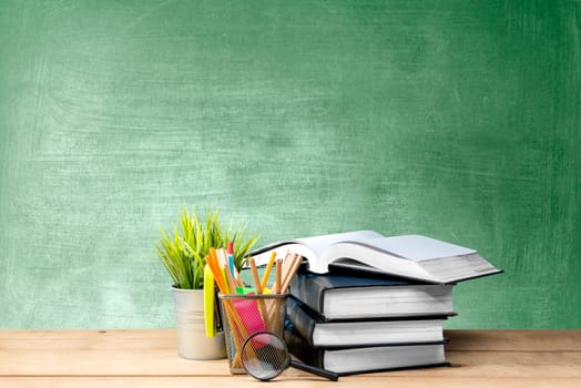 Pile of books with potted plant and pencils in basket container with magnifying glass on the wooden table with chalkboard background. Back to School concept