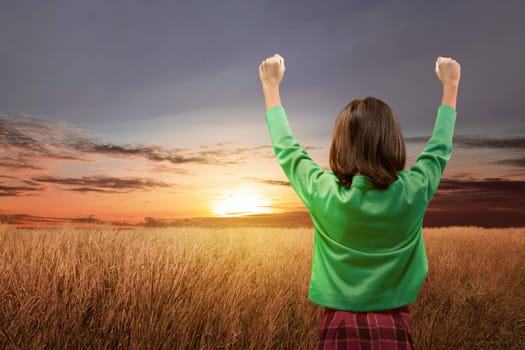 Rear view of asian cute girl standing while raised arms on the meadow field over sunset background. Back to School concept