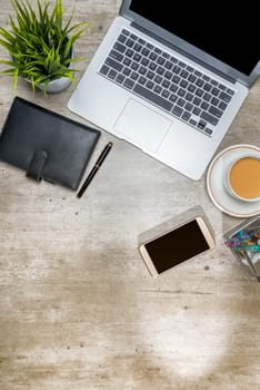 Top view of business desk with laptop, mobile phone, coffee, potted plant, notebook and business accessories on the office