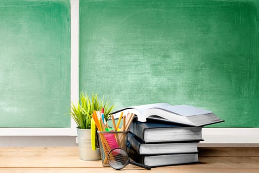 Pile of books with potted plant and pencils in basket container with magnifying glass on the wooden table with chalkboard background. Back to School concept