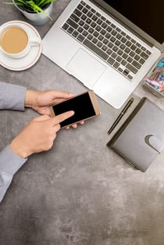 Top view of businessman using mobile phone with laptop, coffee, potted plant, notebook and business accessories on the office desk