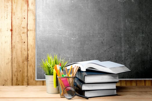 Pile of books with potted plant and pencils in basket container with magnifying glass on the wooden table with blackboard background. Back to School concept