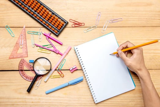 Student writing in notebook with school supplies and stationery on the wooden table. Back to School concept