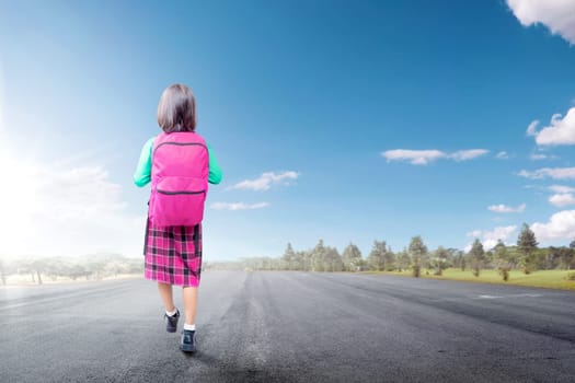 Rear view of asian cute girl with pink backpack walking on the street going to school with blue sky background. Back to School concept