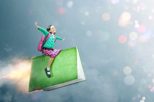 Asian cute girl with glasses and backpack sitting on the book with dramatic sky background. Back to School concept