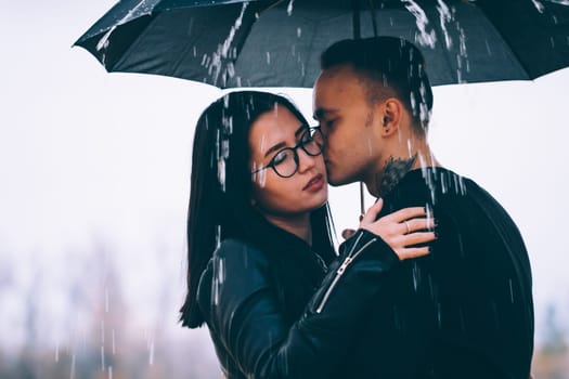 young couple standing under a dark umbrella.