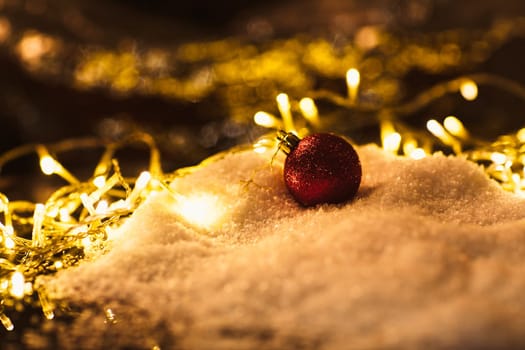 red Christmas ball and luminous garland on the snow.