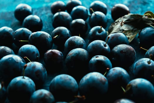 many fresh plums on blue background close up