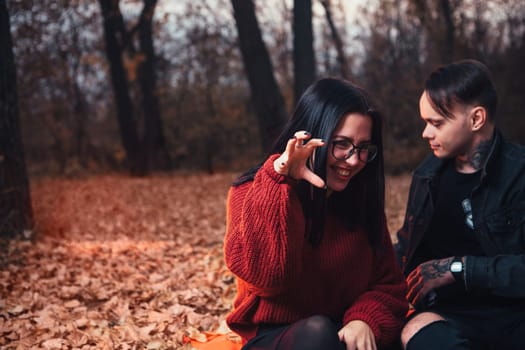 young man and young woman are sitting on a plaid in an autumn forest.