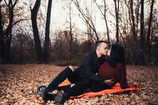 young man and young woman are sitting on a plaid in an autumn forest.