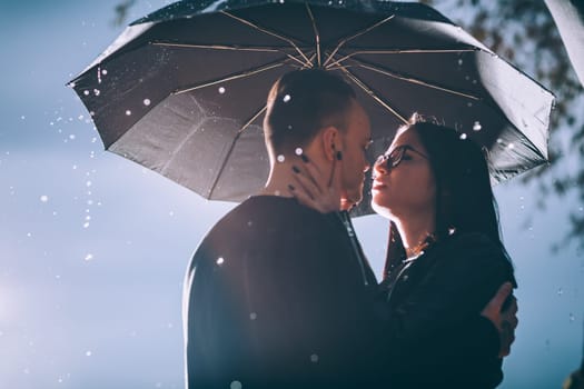young couple standing under a dark umbrella.