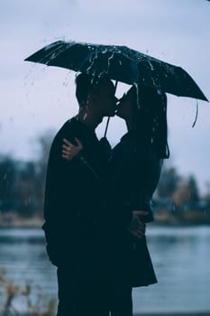 young couple standing under a dark umbrella.