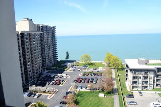 An aria view from an 19 story high rise condominium building of the.parking lot and the lake Ontario on a sunny spring day.