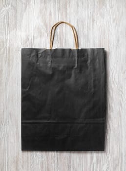 Black paper bag on light wood table background. Responsive design mockup. Flat lay.