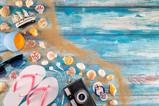 Beach accessories retro film camera sunglasses flip flop and sea shell on wooden. Top view of beach accessories on blue plank summer holiday banner travel concept. Focus on shells.