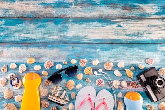 Beach accessories retro film camera sunglasses flip flop and sea shell on wooden. Top view of beach accessories on blue plank summer holiday banner travel concept. Focus on shells.