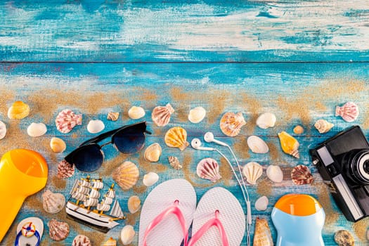 Beach accessories retro film camera sunglasses flip flop and sea shell on wooden. Top view of beach accessories on blue plank summer holiday banner travel concept. Focus on shells.