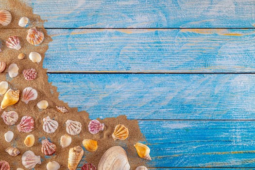 Summer time concept with sea shells on a blue wooden background and sand. Seashells frame on wooden background nautical border. Focus on seashells.