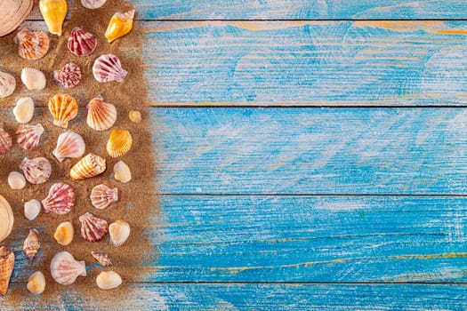 Summer time concept with sea shells on a blue wooden background and sand. Seashells frame on wooden background nautical border. Focus on seashells.
