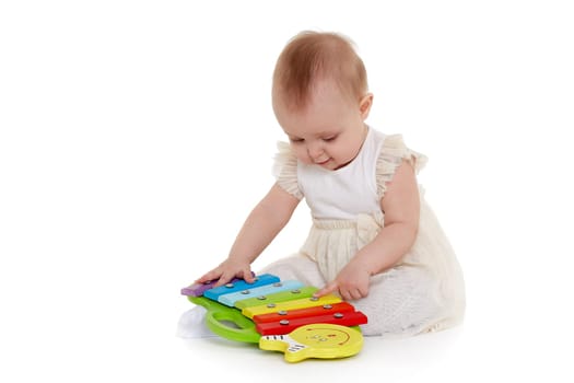 Sweet baby in dress plays with colourful xylophone (musical instrument toy for children) on a white background. Early development and learning toys. Eight months