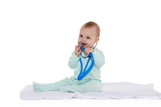 Sweet baby wearing green romper suit sits with blue stethoscope on a white background. Eight months