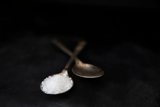 Salt crystals in metal spoons on black background.