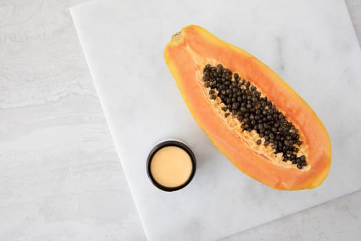 Half a papaya on a marble surface with small jare of papaya extract cream.