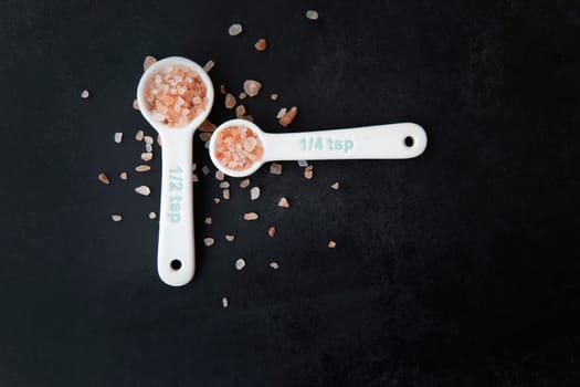 Pink Himalayan salt in measuring spoons on black background.